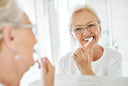 A lady brushing her teeth in the mirror looking at her reflection
